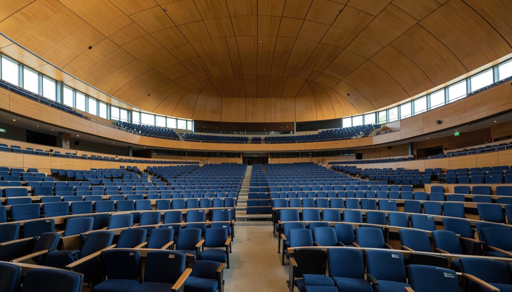 A wide-angle view of the European Parliament hemicycle in Strasbourg, with rows of empty blue seats under a curved ceiling